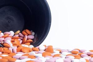Colorful pills spilling out of black plastic container isolated on white background. photo