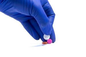 Hand in blue glove holding a pill isolated on white background photo