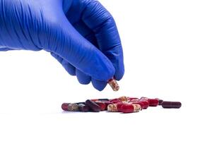 Hand in blue glove picking up a red pill isolated on white background. photo