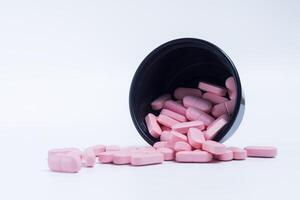 Pink pills spilling out of a black plastic container on a white background. photo