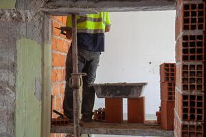 A construction worker applies cement to brick walls during a renovation project, showcasing precision and craftsmanship in a dynamic job site setting. photo