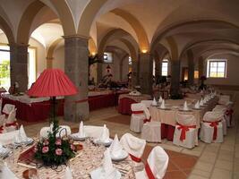A wedding reception setup in a historic convent cloister, featuring elegant table arrangements, floral decorations, and ambient lighting under ancient arches, creating a romantic and timeless atmosphe photo