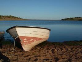 A serene boat docked on the tranquil shores of Alqueva Dam in Alentejo, Portugal, with vast blue waters and lush landscapes in the background. photo