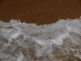 Waves crash onto the sandy shore, creating a burst of white foam. The dynamic movement and contrast capture the essence of the ocean's raw power and beauty. photo