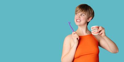 A young white woman with an amazing smile, a toothbrush and a jaw model in her hands on a blue background. A place for your text. photo