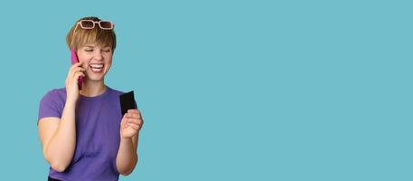 An enthusiastic pretty modern girl advertises mobile banking, online shopping, holds a credit card in her hands and talks on a smartphone. Panoramic image photo