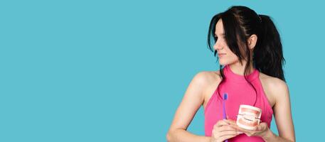 A young Caucasian brunette woman with a toothbrush and a jaw model on a blue background. A panoramic banner with a place for your text. photo