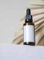 Cosmetic amber glass bottle with white lable down up on table and dry palm leaf on white background. photo