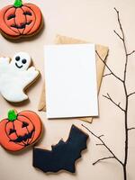 Empty white postcard and craft envelope and Halloween gingerbread cookies - Jack O'Lantern, bat and ghost on beige background photo