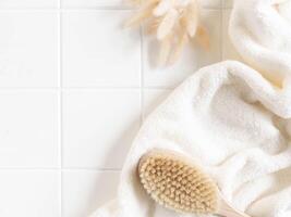 Bath background flat lay with white towels, wood brush and dry flowers on white tiles background photo