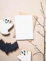 Empty white postcard and craft envelope and Halloween gingerbread cookies - bat and ghosts on beige background. photo