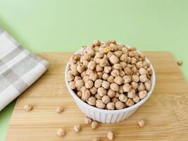 Raw dry chickpea in small ceramic bowl on green background. Traditional ingredient for cooking hummus. Middle Eastern and Mediterranean cuisine. Selected focused photo