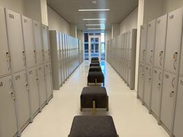 The new lockers, each with a closed steel door, are in two stacked rows and there are chairs lined up in the middle in the new locker room for office staff and visitors. For storage and security photo