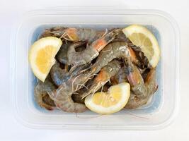 Healthy food. Fresh raw shrimps with lemon in a plastic container photo