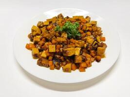 Oseng Tempe and Tofu is Indonesian stir-fried tempeh, tofu and carrot seasoned with shallots, garlic, salt, bay leaf, galangal and sweet soy sauce served on white plate photo