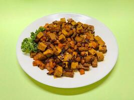 Oseng Tempe and Tofu is Indonesian stir-fried tempeh, tofu and carrot seasoned with shallots, garlic, salt, bay leaf, galangal and sweet soy sauce served on white plate photo
