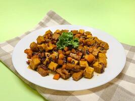 Oseng Tempe and Tofu is Indonesian stir-fried tempeh, tofu and carrot seasoned with shallots, garlic, salt, bay leaf, galangal and sweet soy sauce served on white plate photo