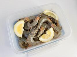 Healthy food. Fresh raw shrimps with lemon in a plastic container photo