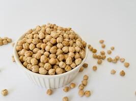 Raw dry chickpea in small ceramic bowl on white background. Traditional ingredient for cooking hummus. Middle Eastern and Mediterranean cuisine. Selected focused photo