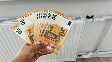 Close-up of a woman hands with banknotes of money in her hands next to a heating radiator. Increase in heating prices in selected households in Europe photo