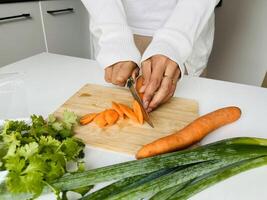 Cooking concept. Unrecognizable woman in white clothes making healthy dinner, cropped of lady preparing delicious meal at home, cutting vegetables on chopping board, kitchen interior, close up photo