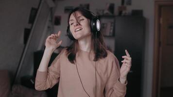 A beautiful girl in big headphones listens to music and dances beautifully dynamically in her room. Freedom. Emancipation. Favorite music. Emancipation. In rhythm. Beautiful lighting. Cinema light. video