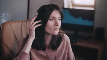 A beautiful girl with headphones listens to music in a chair at the computer and sings, smiles. The equalizer is playing on the monitor. Shakes his head to the beat and beats with his finger. video