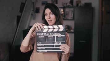 A beautiful girl holds a Clapperboard in her hands. Claps. Clicks. Winks at the camera. Flirting, flirting. The movie has started. The beginning of filming. Action. Slow Motion video
