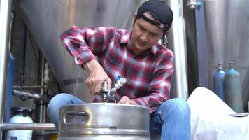 A handsome man is assembling or repairing beer tanks for homemade beer production behind a large brewing tank. video