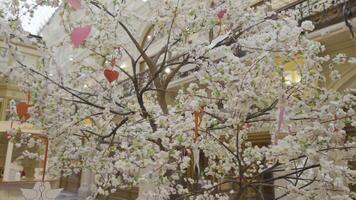 Close up of beautiful blooming artificial tree in a shopping center. Action. Tree branches decorated by hearts, view inside of a shopping mall. video