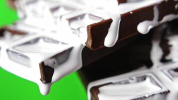 Close-up of chocolate with white cream. Stock clip. White liquid cream flows down chocolate bar. Sweet chocolate with cream on green background video