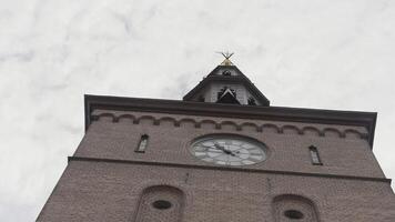 A huge chapel. Action.A large long tower made of dark stone with a large clock on top and behind you can see the blue sky. video