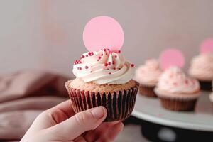 a person holding up a cupcake with pink frosting, photo