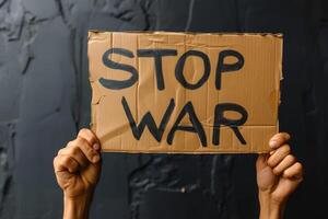 a person holding up a cardboard sign with stop war written, photo