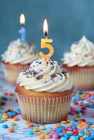 small cupcakes sit on white paper with lit candles burning, photo