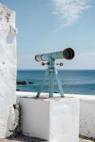 an outdoor telescope set on the wall by some water, photo