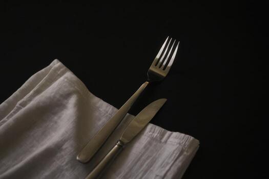two knifes with forks and napkin resting on dark background, photo