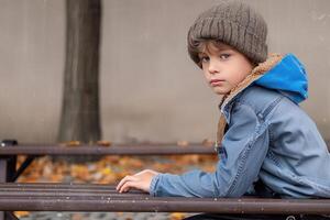 the young boy is sitting on the park bench, photo