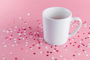 a coffee mug with heart - shaped confetti sitting on pink surface, photo