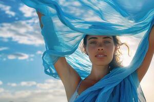 the woman is wearing a blue scarf in a beach location looking at the camera, photo