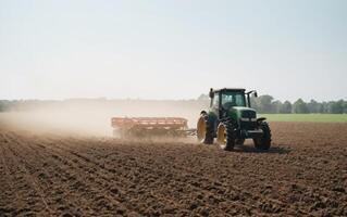a tractor plowing an empty field with dust, photo