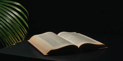 an open book on top of a table next to green leaves, photo