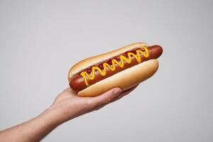 man's hand holding mustard in white bun over gray background, photo