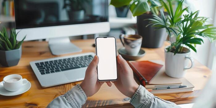 a man holds an iphone near an empty desk with coffee, photo