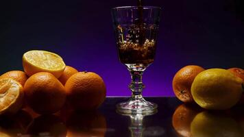 Rum drink being poured into long glass, isolated on colorful lighted wall background. Stock clip. Alcohol drink on the reflective table or bar counter with orange fruits. video