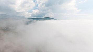 Top view of thick clouds with mountain peak on horizon. Schot. Flying in cloudy sky with dense clouds from top of mountain. Landscape of top of green mountain on horizon among white clouds video