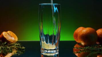 Drink with oranges and bright light on background is poured into glass. Stock clip. Bar atmosphere and alcoholic drink with fruit. Carbonated drink with fruit around is poured into transparent drink video