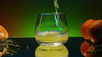 Citrus cocktail on the glass surface of a table. Stock clip. Fruits and rosemary leaves lying on the table on colorful lighted wall background. video