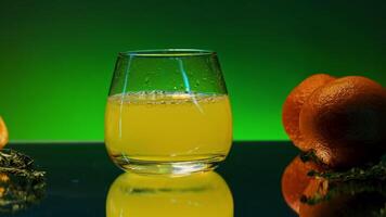 Drop falling into orange juice. Stock clip. Orange juice with alcohol in glass on isolated background. Alcoholic drink with juice and oranges in bar video