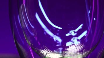 Close up of empty transparent glass being filled with green soda water. Stock clip. Wall with colorful illumination of a night bar. video